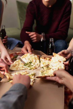 A pizza party, a group of friends chatting and happily eating pizza at the table and drinking sweet soda water. Top view from the second floor. High quality photo